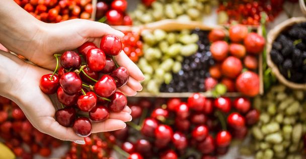 fresh cherry in the hands of a girl, against a background of different fruits, the concept of healthy nutrition and vitamins - Фото, зображення