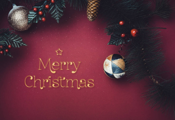 Golden sparkle Merry Christmas text with star with ball and fir branches for wreath with cherry and pine cone on dark red background. greeting card for winter holiday festive celebration concept - Photo, image
