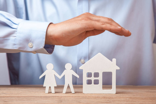 Versicherung einer jungen Familie und eines Hauses. Mann im Hemd bedeckt seine Hände mit zwei Männern und Frau und Haus - Foto, Bild