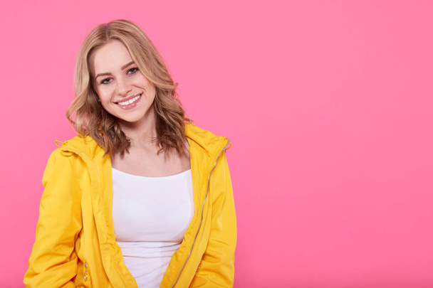 Beautiful smiling trendy teenage girl in bright yellow jacket looking at camera. Attractive young woman portrait over pastel pink background. Confident teenager concept. - Valokuva, kuva