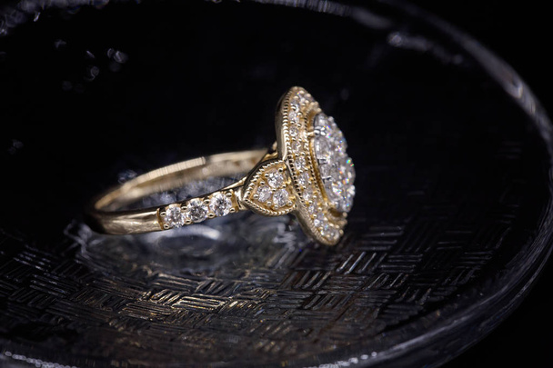 Um halo de diamantes em torno de um aglomerado central de diamantes definido em um anel de ouro amarelo isolado em um fundo preto
 - Foto, Imagem