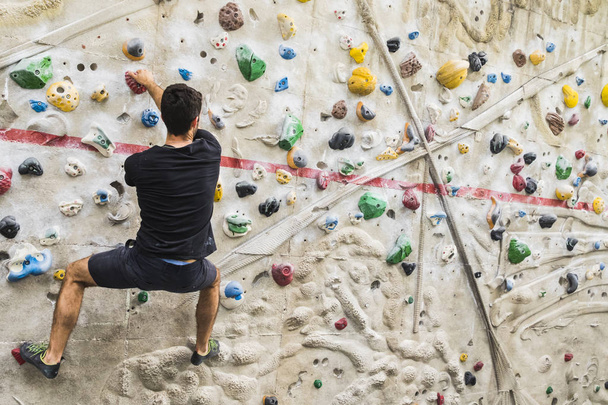 Un hombre practicando escalada en roca en paredes artificiales en interiores. Estilo de vida activo y concepto de bouldering
. - Foto, Imagen