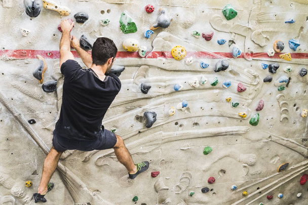 A Man practicing rock climbing on artificial wall indoors. Active lifestyle and bouldering concept. - Photo, Image
