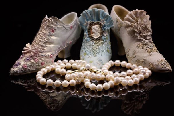 Joukko kiiltäviä perintökalleuksia laadukkaita helmiä vanhanaikaisten koristeltujen koristeellisten pienoiskeraamisten kenkien edessä
 - Valokuva, kuva