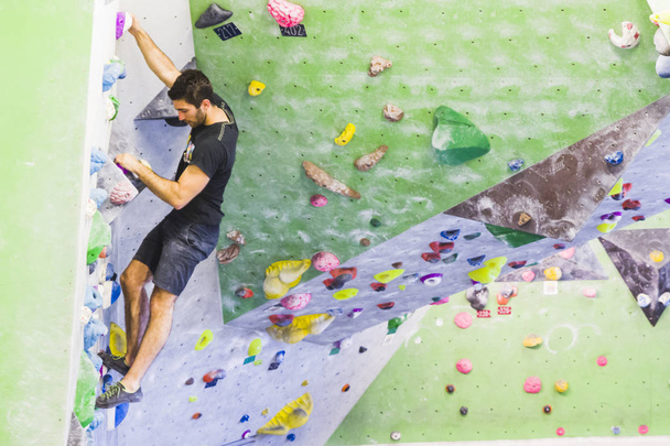 A Man practicing rock climbing on artificial wall indoors. Active lifestyle and bouldering concept. - Photo, Image