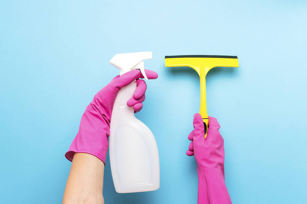 Žena v růžové gumové rukavice drží škrabku pro čištění oken a sprej pro čištění na modrém pozadí. Koncepce čištění služby. Plochá ležel, horní pohled. - Fotografie, Obrázek