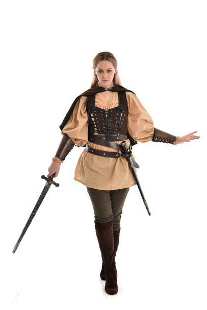 retrato de longitud completa de chica rubia con traje de guerrero medieval marrón. pose de pie, aislado sobre fondo blanco del estudio
. - Foto, imagen