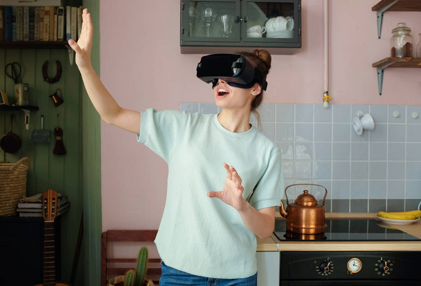 Mujer bonita joven usando gafas de realidad virtual para jugar video juego interior en el acogedor interior de la cocina colorida de moda
 - Foto, imagen