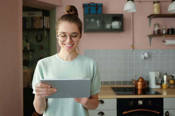 Closeup shot of young smiling woman wearing trendy round eyeglasses, holding gray tablet, using mobile app, buying products on-line - Fotoğraf, Görsel