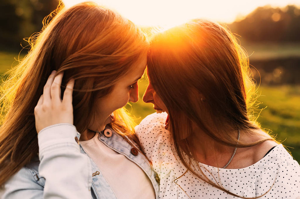 funny girls leaned their heads to each other and open their mouths against the backdrop of evening nature and the sunset - Foto, Imagen