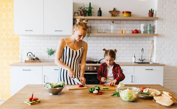 Photo of beautiful woman with her daughter cutting vegetables in kitchen - Φωτογραφία, εικόνα