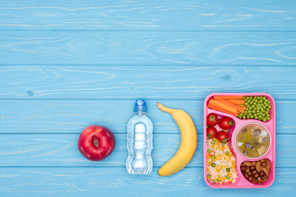 elevated view of tray with kids lunch for school, bottle of water and fruits on blue table - Photo, Image