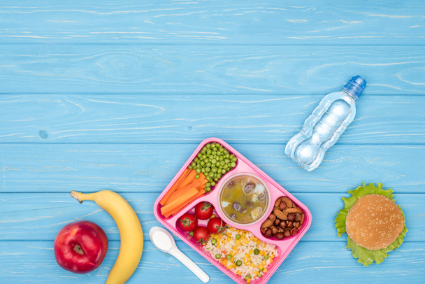 top view of tray with kids lunch for school, bottle of water and fruits on blue wooden surface - Photo, Image