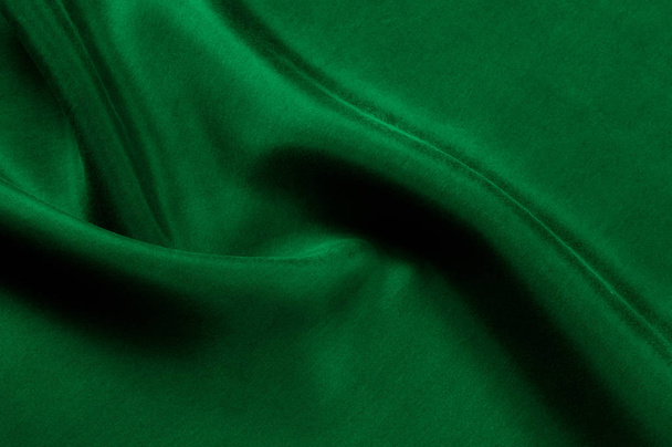 Background texture, pattern. Thick thick silk fabric is green. This satin fabric is ideal for creating a smooth flow in design, it has a liquid drape and exquisite shine. - Photo, Image
