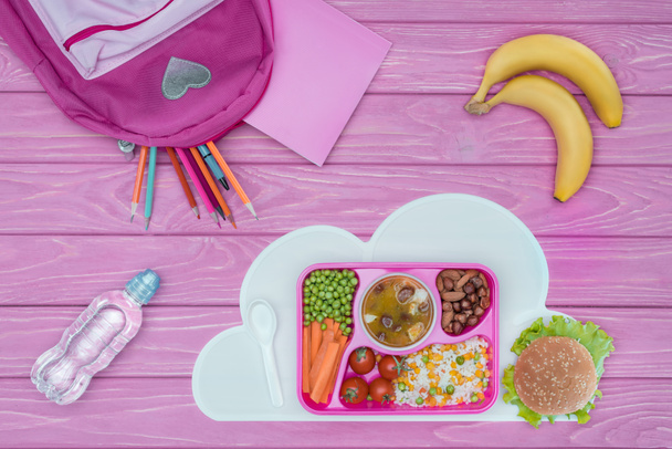 top view of tray with kids lunch for school, pink bag, pencils and bananas on pink table - Fotografie, Obrázek
