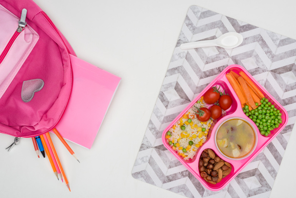 κάτοψη του δίσκος με μεσημεριανό γεύμα τα παιδιά για το σχολείο και ροζ τσάντα με μολύβια σε λευκά επιτραπέζια - Φωτογραφία, εικόνα