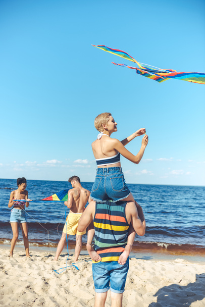 selective focus of interracial group of friends with kites having fun on sandy beach - Zdjęcie, obraz