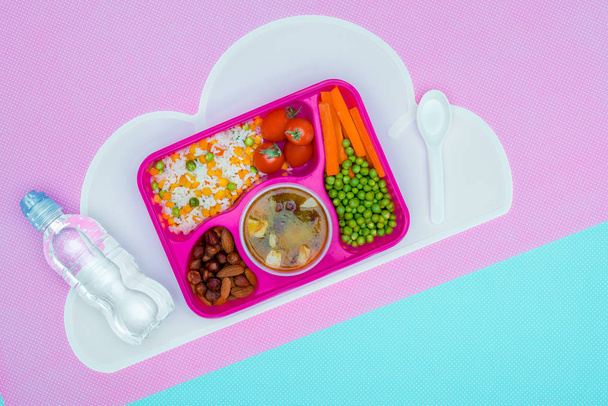 vista superior de la bandeja con almuerzo para niños para la escuela y botella de agua en la mesa violeta y azul
 - Foto, Imagen