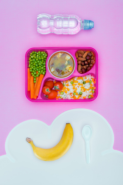 top view of tray with kids lunch for school, bottle of water and banana on violet table - Фото, изображение