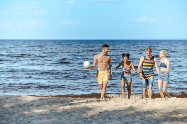 amici multiculturali con pallavolo passeggiando sulla spiaggia sabbiosa
 - Foto, immagini