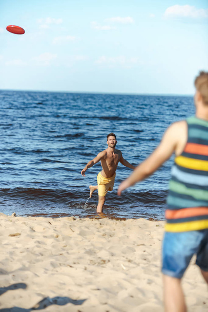 selective focus of young men playing with flying disc on sandy beach - Photo, Image