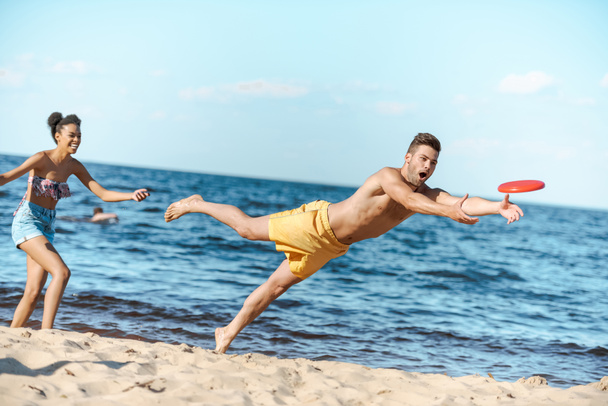 giovane coppia multiculturale che gioca con disco volante sulla spiaggia il giorno d'estate
 - Foto, immagini