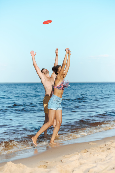 joven pareja multicultural jugando con disco volador en la playa en el día de verano
 - Foto, imagen