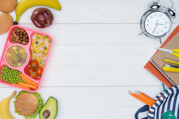top view of kids lunch for school and alarm clock with bag on wooden table - 写真・画像
