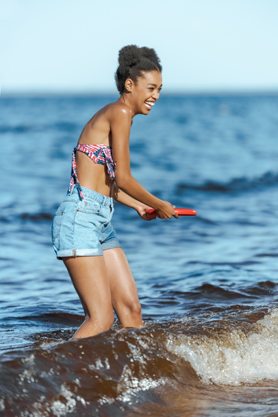 cheerful african american woman with flying disc on beach - Foto, Imagen