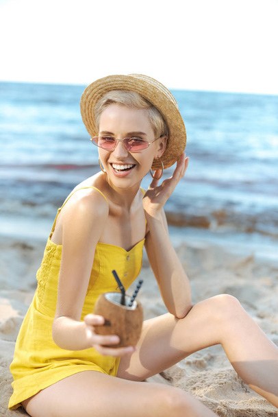 vista parcial de la mujer sosteniendo coctel de coco con pajitas en la mano
 - Foto, Imagen