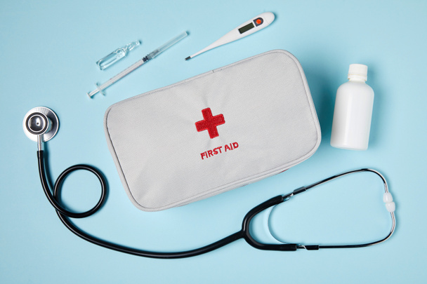 top view of white first aid kit bag with stethoscope and medicines on blue surface - Photo, Image