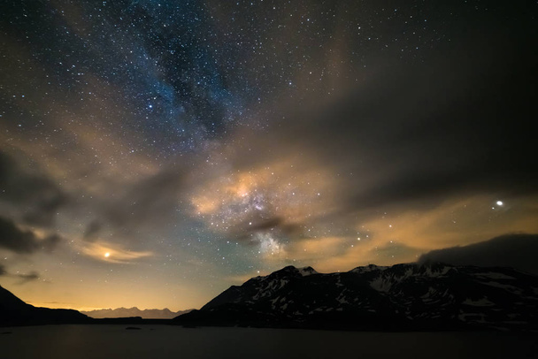 Astro night sky, Milky way galaxy stars over the Alps, stormy sky, motion clouds, snowcapped mountain range and lake - Photo, Image