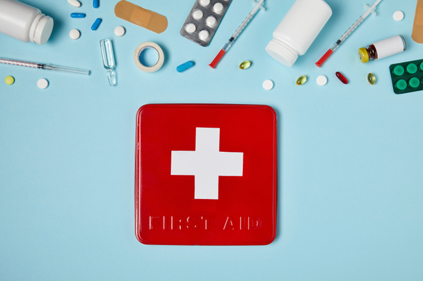 κάτοψη του κόκκινο πρώτων βοηθειών κιτ πλαίσιο σε μπλε επιφάνεια με διάφορα φάρμακα - Φωτογραφία, εικόνα