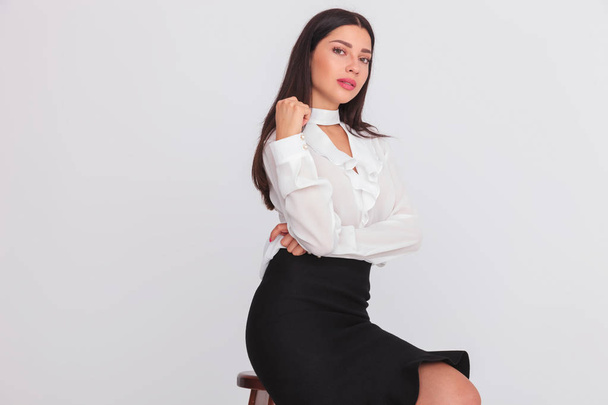 portrait of young seated businesswoman wearing a white shirt and a black dress on light grey background - Fotoğraf, Görsel