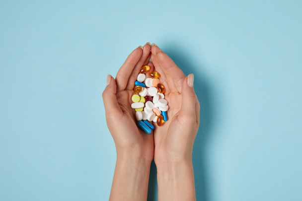 tiro cortado de mulher segurando montão de pílulas sobre a superfície azul
 - Foto, Imagem