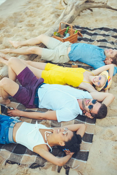 side view of multiracial young people lying on blanket while spending time on sandy beach - Φωτογραφία, εικόνα
