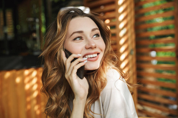 Close up portrait of a smiling young girl talking on mobile phone while sitting in a cafe - Photo, Image
