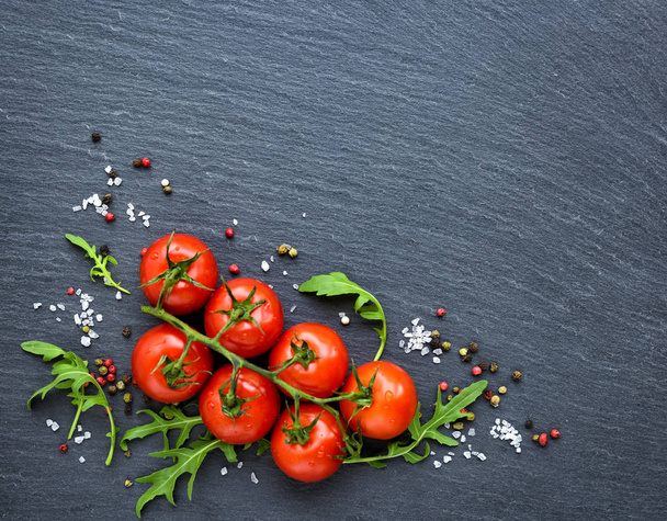 Tomates cerises fraîches, sel, poivre et feuilles de roquette sur une planche d'ardoise noire, vue sur le dessus
 - Photo, image