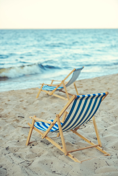 foco seletivo de cadeiras de praia de madeira na praia de areia com mar no fundo
 - Foto, Imagem