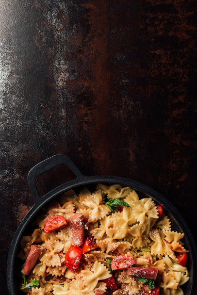 top view of pasta with jamon, cherry tomatoes, mint leaves covered by grated parmesan in pan on table  - Fotografie, Obrázek
