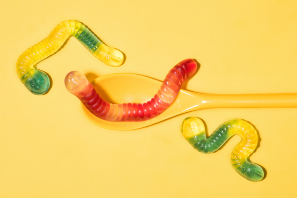bovenaanzicht van heerlijke gummy wormen met lepel op geel - Foto, afbeelding