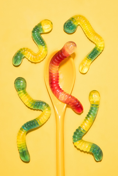 κάτοψη του πολύχρωμο κολλώδης σκουλήκια με κουτάλι στο κίτρινο - Φωτογραφία, εικόνα
