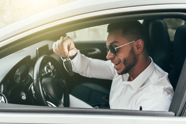 Όμορφος νέος άνδρας που δείχνει τα κλειδιά του αυτοκινήτου του πρόσφατα αγόρασε Auto κάθεται στο πολυτελές όχημα - Φωτογραφία, εικόνα