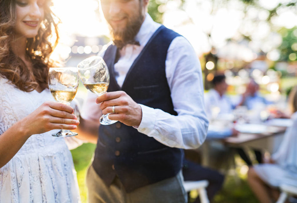 Bride and groom clinking glasses at wedding reception outside in the backyard. - Photo, image
