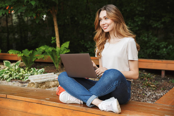 Happy young girl using laptop computer while sitting on a bench outdoors - Foto, immagini