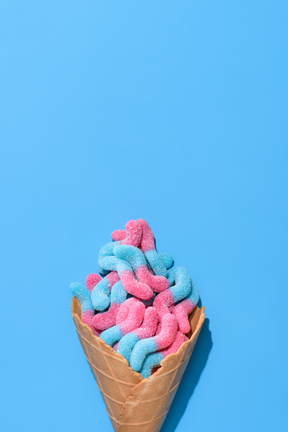bovenaanzicht van zoete gummy wormen in wafel kegel op blauw - Foto, afbeelding