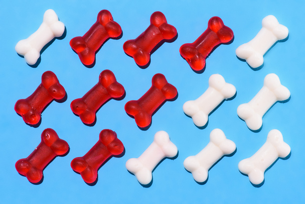 top view of gummy candies in shape of red and white bones composition on blue - Foto, Imagen