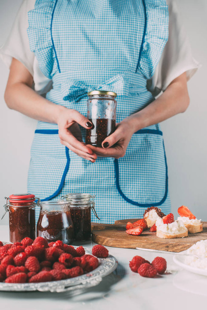 przycięty obraz kobiety w fartuch, trzymając w kuchni słoik z dżemem owoców  - Zdjęcie, obraz