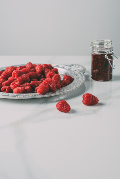 selective focus of silver tray with raspberries and jar of jam on marble table  - Foto, Imagem