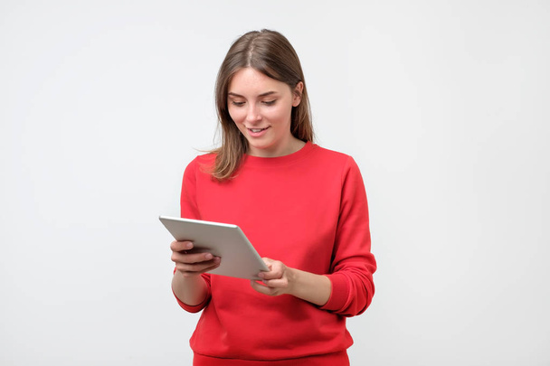 エレガントな若い女性、タブレットを使用して赤いセーターで画面を見ています。近代的な技術を使用して、一般的な日常生活の中で - 写真・画像